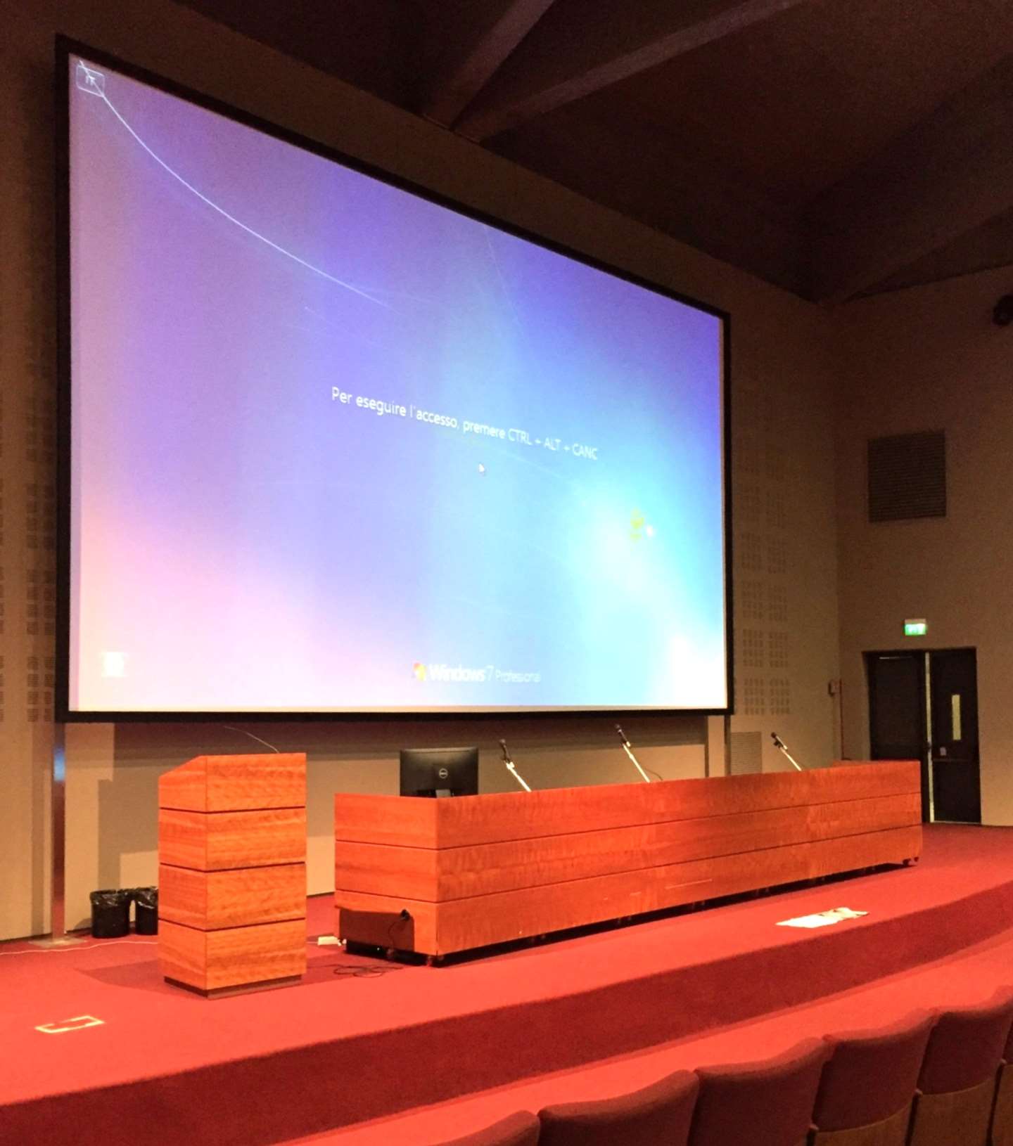 Stage of the Aula Magna CTO showing the wooden chairs' table, podium and large projection screen